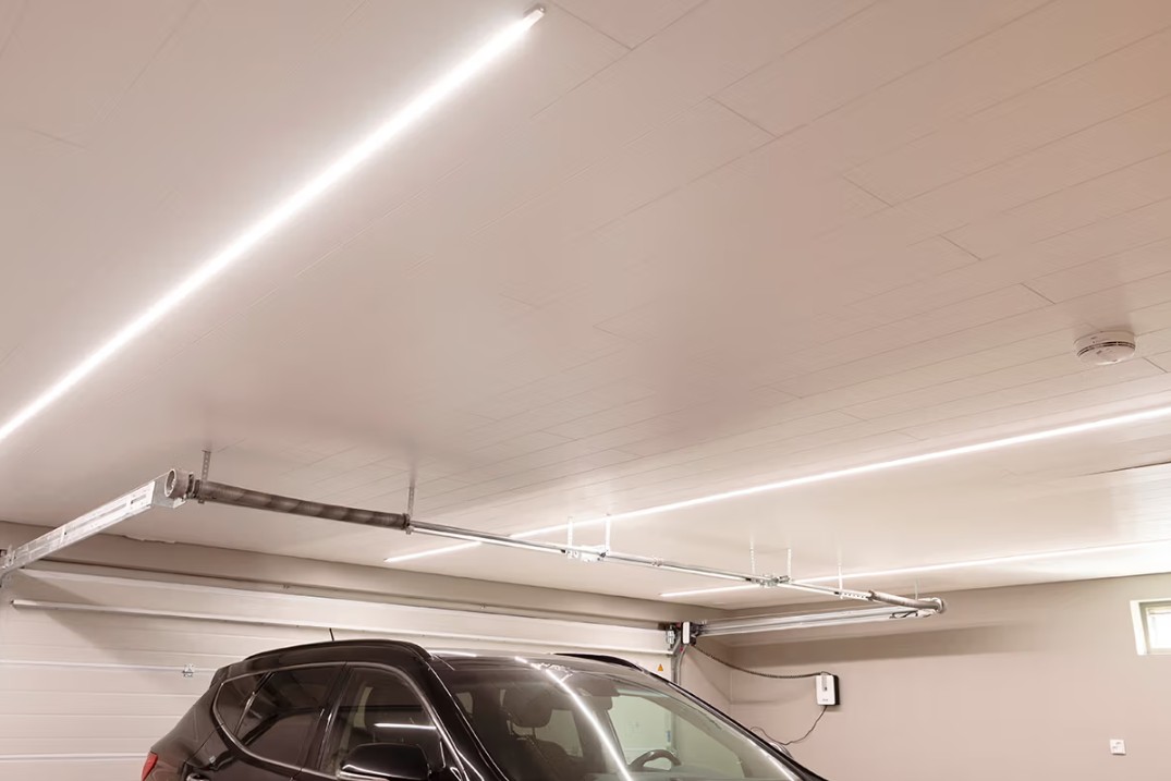 Nykyaikainen autotalli, jossa musta auto on parkissa ja katon kirkkaat LED-nauhat valaisevat tilan tehokkaasti. - LedStore led-nauhatuppoprofiilissa autotallin katossa tasaisesti aseteltuna koko tilaan