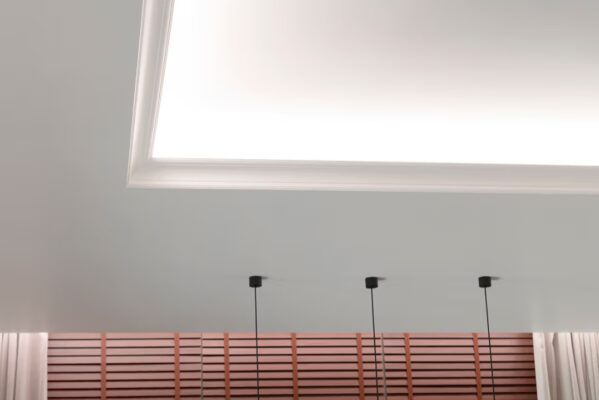 Minimalistinen kattoratkaisu upotetuilla LED-valaistusratkaisuilla, kolme riippuvaa LED-riippuvalaisinta sekä moderni puusäleikköseinä. - LedStore Toimiva valaistuskokonaisuus olohuoneessa. Katon valohyllyllä oleva led-nauhavalaistus valaisee kohti kattoa ja alaspäin kohti verhoja.
