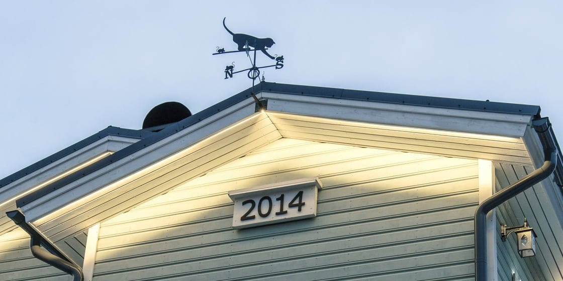 Light blue building with "2014" plaque, cat weather vane on roof, softly lit by LED lights. Perfect for energy-efficient illumination.